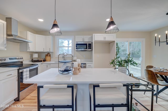 kitchen featuring stainless steel appliances, wall chimney exhaust hood, light countertops, and white cabinetry