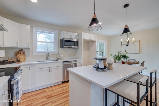 kitchen featuring a sink, white cabinetry, a kitchen breakfast bar, appliances with stainless steel finishes, and light wood-type flooring