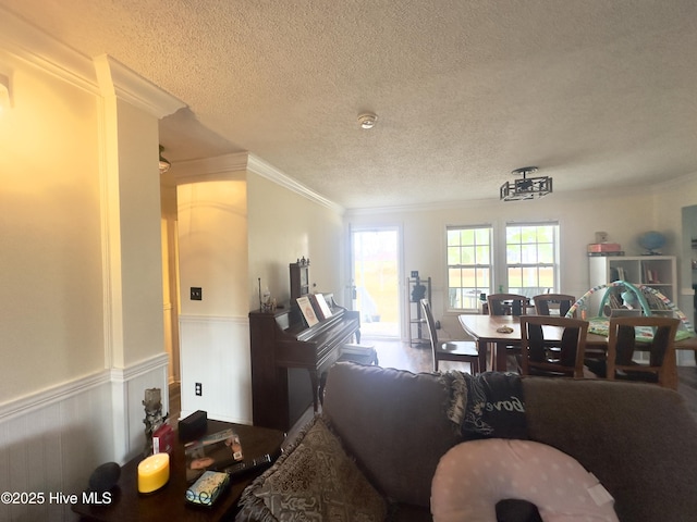 living area with a textured ceiling, ornamental molding, and wainscoting