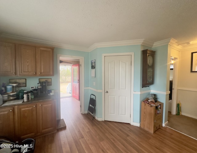 kitchen with baseboards, a textured ceiling, wood finished floors, and ornamental molding