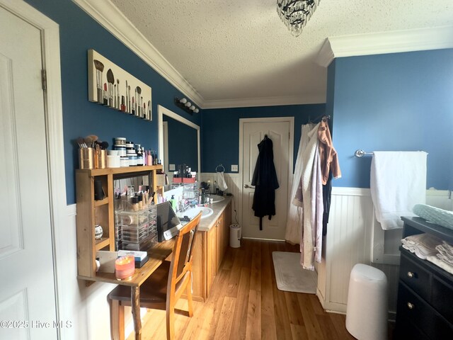 interior space with wood finished floors, wainscoting, a textured ceiling, and ornamental molding