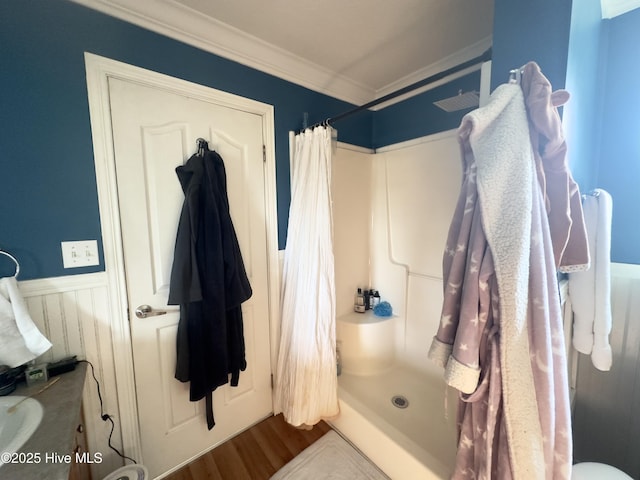 bathroom with a shower with curtain, wood finished floors, a wainscoted wall, and ornamental molding