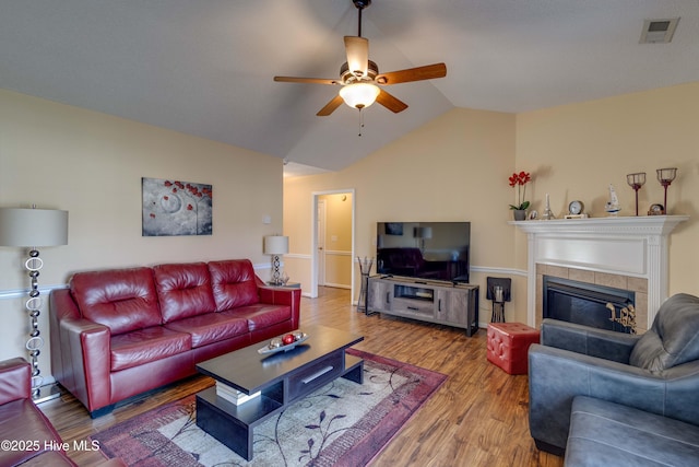 living area with visible vents, ceiling fan, a tiled fireplace, lofted ceiling, and wood finished floors