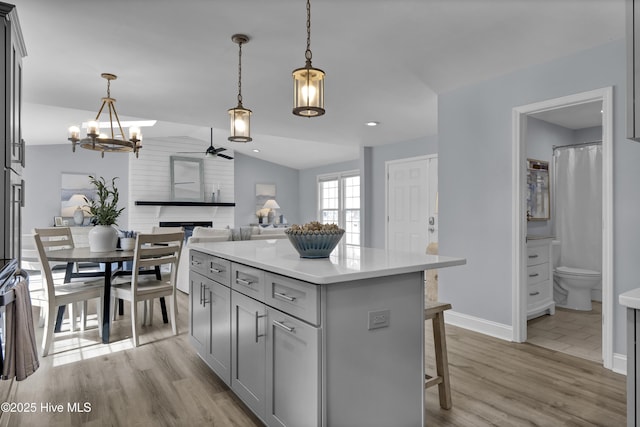 kitchen featuring lofted ceiling, gray cabinets, hanging light fixtures, and light wood-style flooring