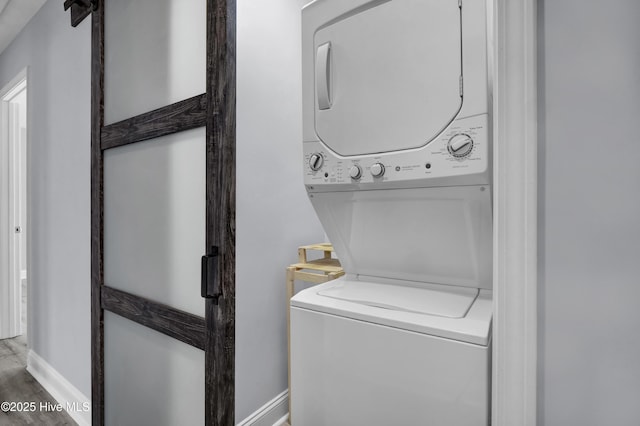 washroom featuring laundry area, baseboards, stacked washing maching and dryer, and wood finished floors