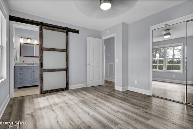 unfurnished bedroom featuring wood finished floors, a barn door, a sink, and visible vents