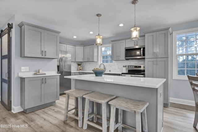 kitchen featuring a barn door, appliances with stainless steel finishes, light countertops, and gray cabinetry