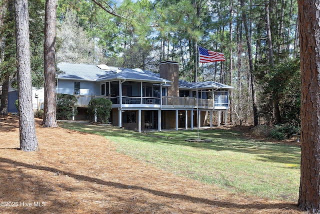 rear view of property with a lawn, a deck, a chimney, and a sunroom