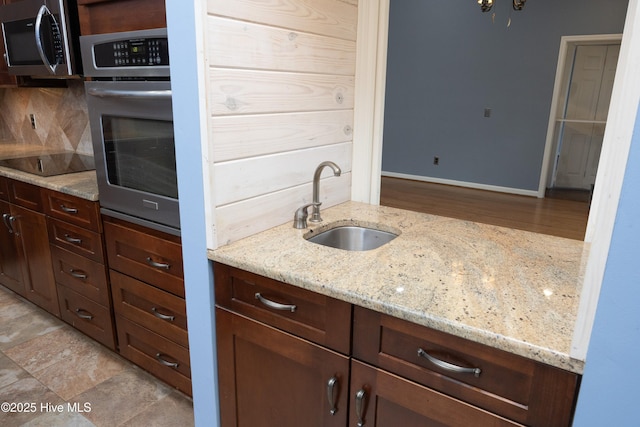 kitchen featuring baseboards, light stone countertops, decorative backsplash, appliances with stainless steel finishes, and a sink