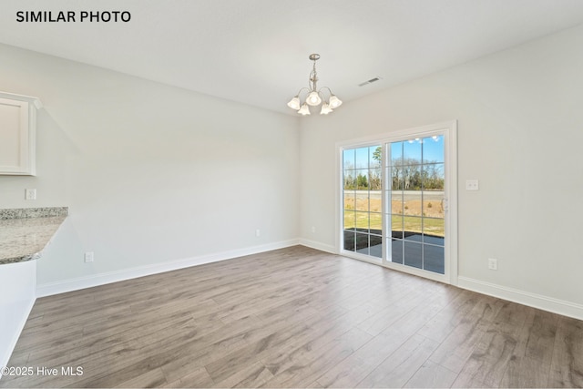 unfurnished dining area featuring a chandelier, visible vents, baseboards, and wood finished floors