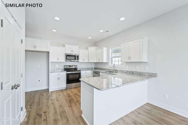 kitchen featuring appliances with stainless steel finishes, a peninsula, light wood-style floors, white cabinets, and a sink