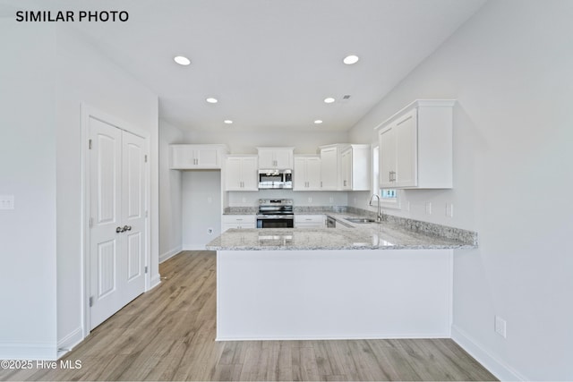 kitchen featuring light stone counters, a peninsula, a sink, stainless steel appliances, and white cabinets