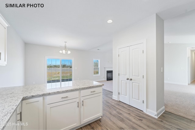 kitchen with baseboards, an inviting chandelier, white cabinets, a glass covered fireplace, and open floor plan