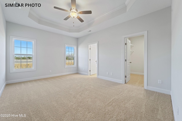 unfurnished bedroom with a walk in closet, light carpet, a raised ceiling, crown molding, and baseboards