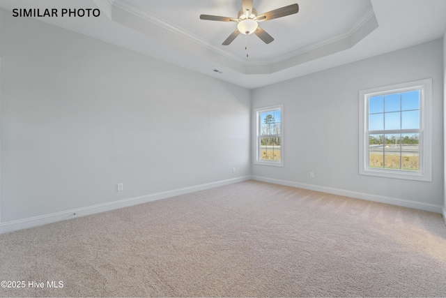 empty room with a tray ceiling, light carpet, baseboards, and ornamental molding