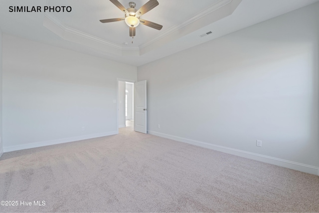 carpeted empty room with a tray ceiling, baseboards, visible vents, and crown molding