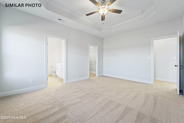 unfurnished bedroom featuring visible vents, a walk in closet, ornamental molding, carpet flooring, and a raised ceiling