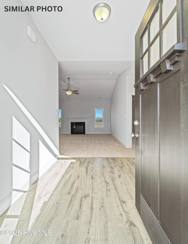 foyer featuring baseboards, lofted ceiling, a fireplace, wood finished floors, and a ceiling fan