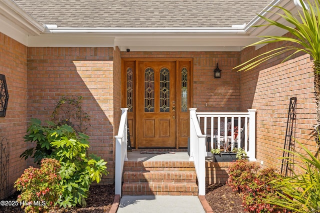 doorway to property featuring a porch, brick siding, and a shingled roof