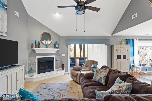 living area with visible vents, lofted ceiling, a fireplace with raised hearth, and ceiling fan