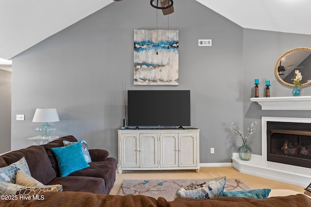 living area featuring baseboards, lofted ceiling, light colored carpet, and a fireplace with raised hearth