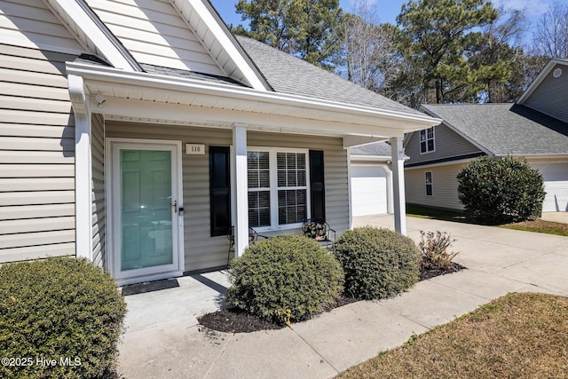 view of exterior entry featuring concrete driveway, an attached garage, and a shingled roof