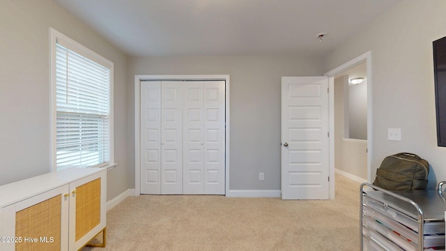 bedroom with baseboards, a closet, and light colored carpet