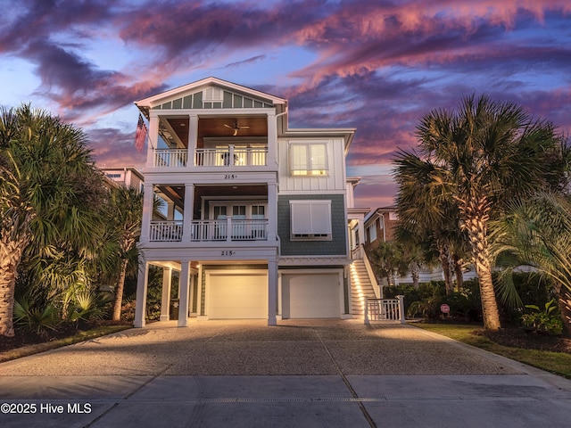 beach home featuring board and batten siding, a ceiling fan, a balcony, a garage, and driveway