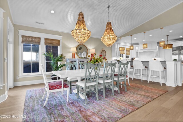 dining space with lofted ceiling, visible vents, light wood-style floors, an inviting chandelier, and crown molding