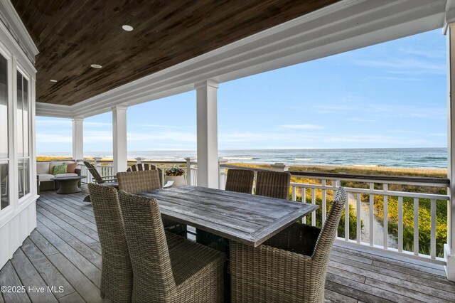 wooden deck with outdoor dining space, a beach view, and a water view