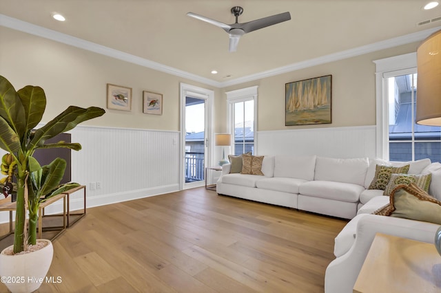 living area with light wood-style floors, a wainscoted wall, visible vents, and ornamental molding