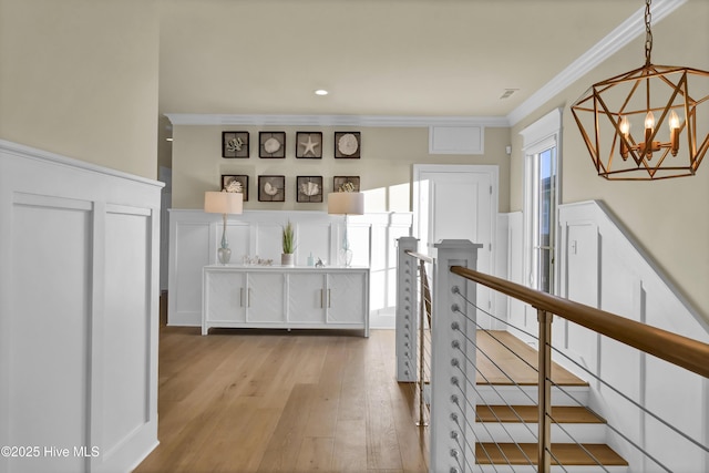 hall featuring wood-type flooring, crown molding, an upstairs landing, a decorative wall, and a notable chandelier