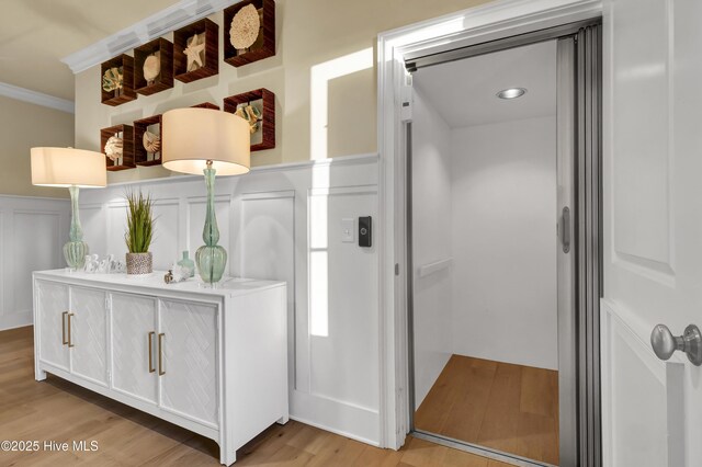 interior space with elevator, a decorative wall, wood finished floors, and wainscoting