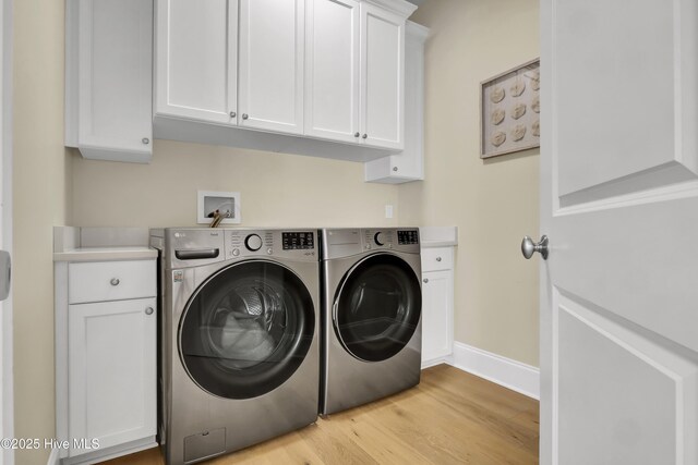 clothes washing area with cabinet space, light wood-style flooring, baseboards, and washer and clothes dryer