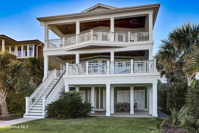 view of front facade featuring a balcony, a patio area, stairway, and a front yard