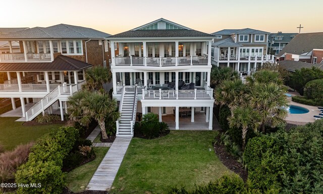 rear view of house featuring a balcony, stairs, an outdoor pool, and a lawn