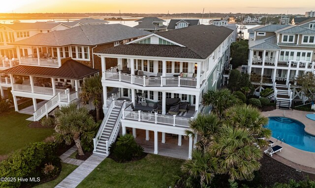 back of house at dusk with a shingled roof, a residential view, an outdoor pool, and stairway