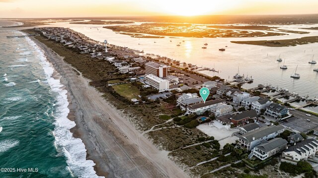 aerial view at dusk featuring a view of the beach and a water view