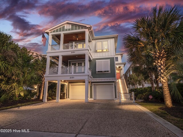 coastal inspired home with a ceiling fan, board and batten siding, a balcony, driveway, and stairs