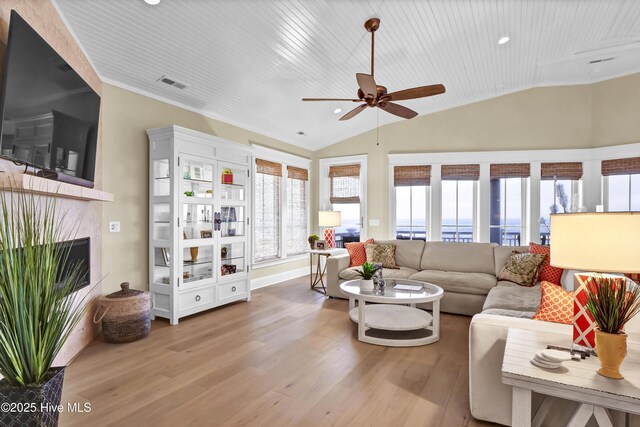 living room featuring lofted ceiling, visible vents, a tiled fireplace, a ceiling fan, and wood finished floors