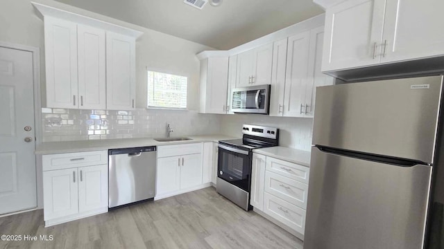 kitchen featuring stainless steel appliances, light countertops, a sink, and white cabinetry