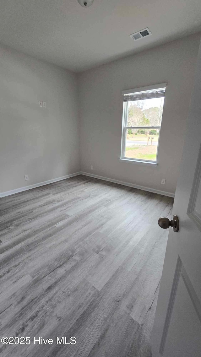 spare room with wood finished floors, visible vents, and baseboards