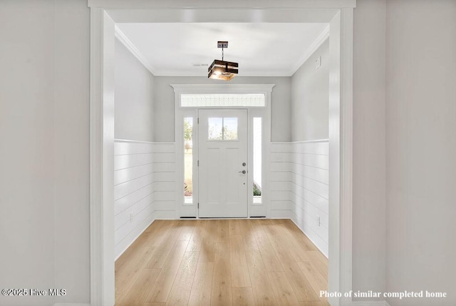 foyer entrance with a wainscoted wall, crown molding, and light wood finished floors