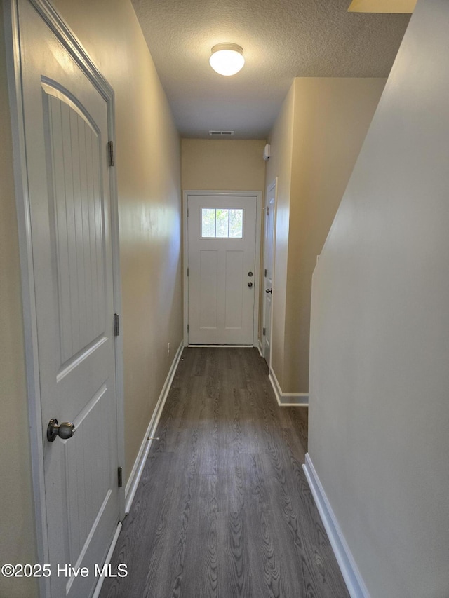 doorway to outside with a textured ceiling, dark wood-type flooring, visible vents, and baseboards