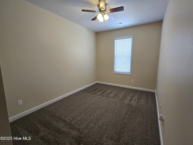 spare room with a ceiling fan, dark colored carpet, visible vents, and baseboards