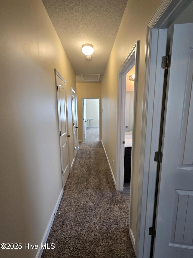 hall with visible vents, carpet flooring, a textured ceiling, and baseboards