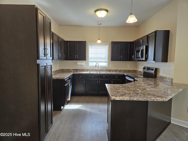 kitchen with a peninsula, a sink, light wood-style floors, hanging light fixtures, and appliances with stainless steel finishes