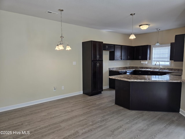 kitchen with visible vents, baseboards, light wood-style flooring, hanging light fixtures, and light stone countertops