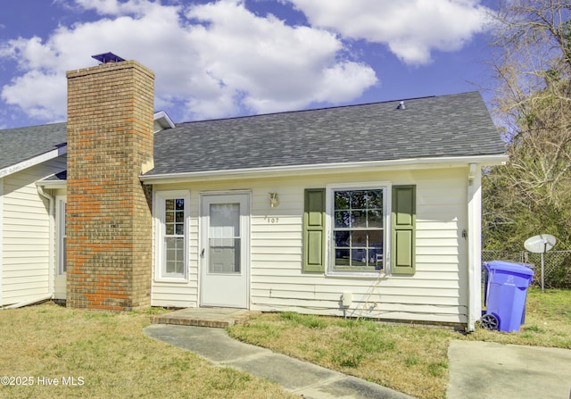 view of front of house with a shingled roof, a chimney, and a front lawn