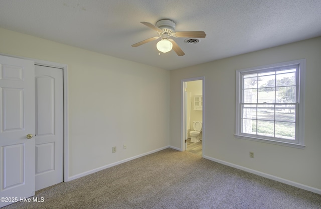 unfurnished bedroom featuring ensuite bathroom, a textured ceiling, carpet floors, visible vents, and baseboards